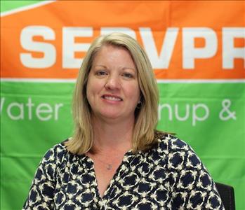 Woman with short blonde hair wearing a black and white shirt in front of a SERVPRO banner