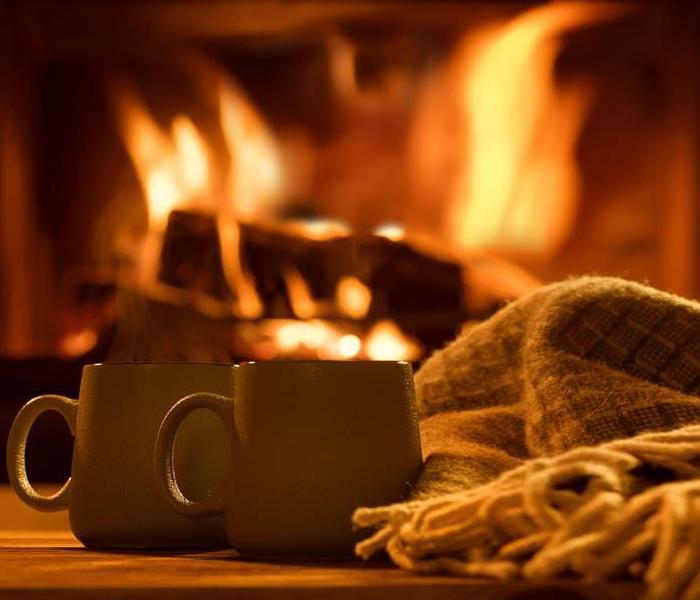 Photo of a fireplace burning with a cozy blanket and two presumably steaming mugs on the table in the forground of the photo 